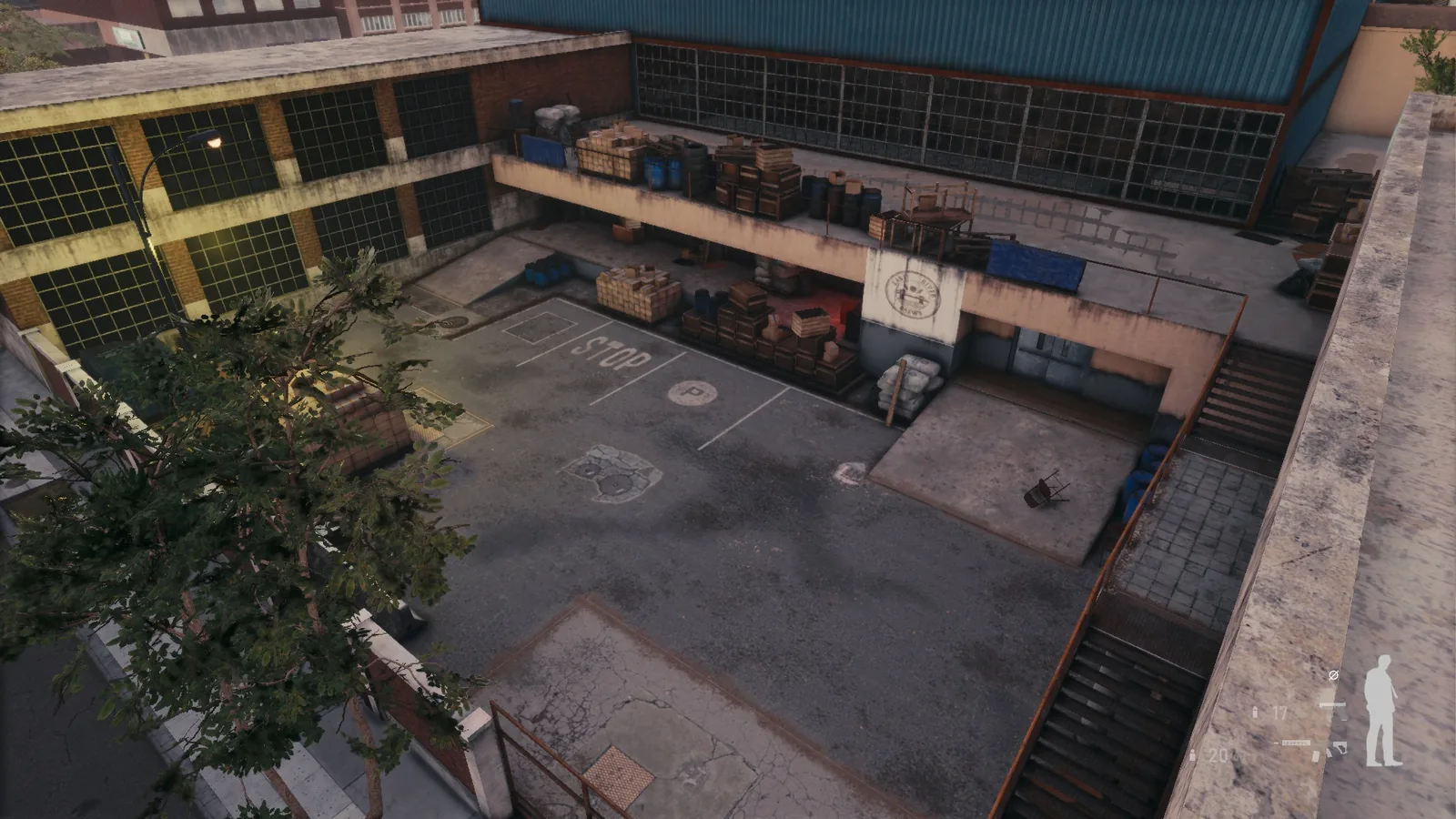Aerial view of a BLACKWOOD courtyard, with a tree, stairs, painted ground markings and an upper walkway of crates