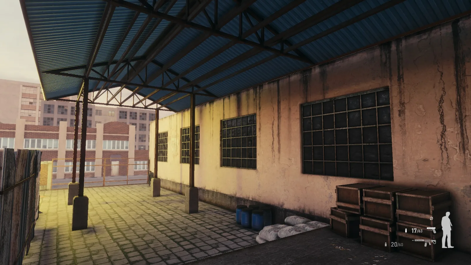Covered loading area outside the BLACKWOOD warehouse, with steel trusses, stacked crates and brick buildings beyond