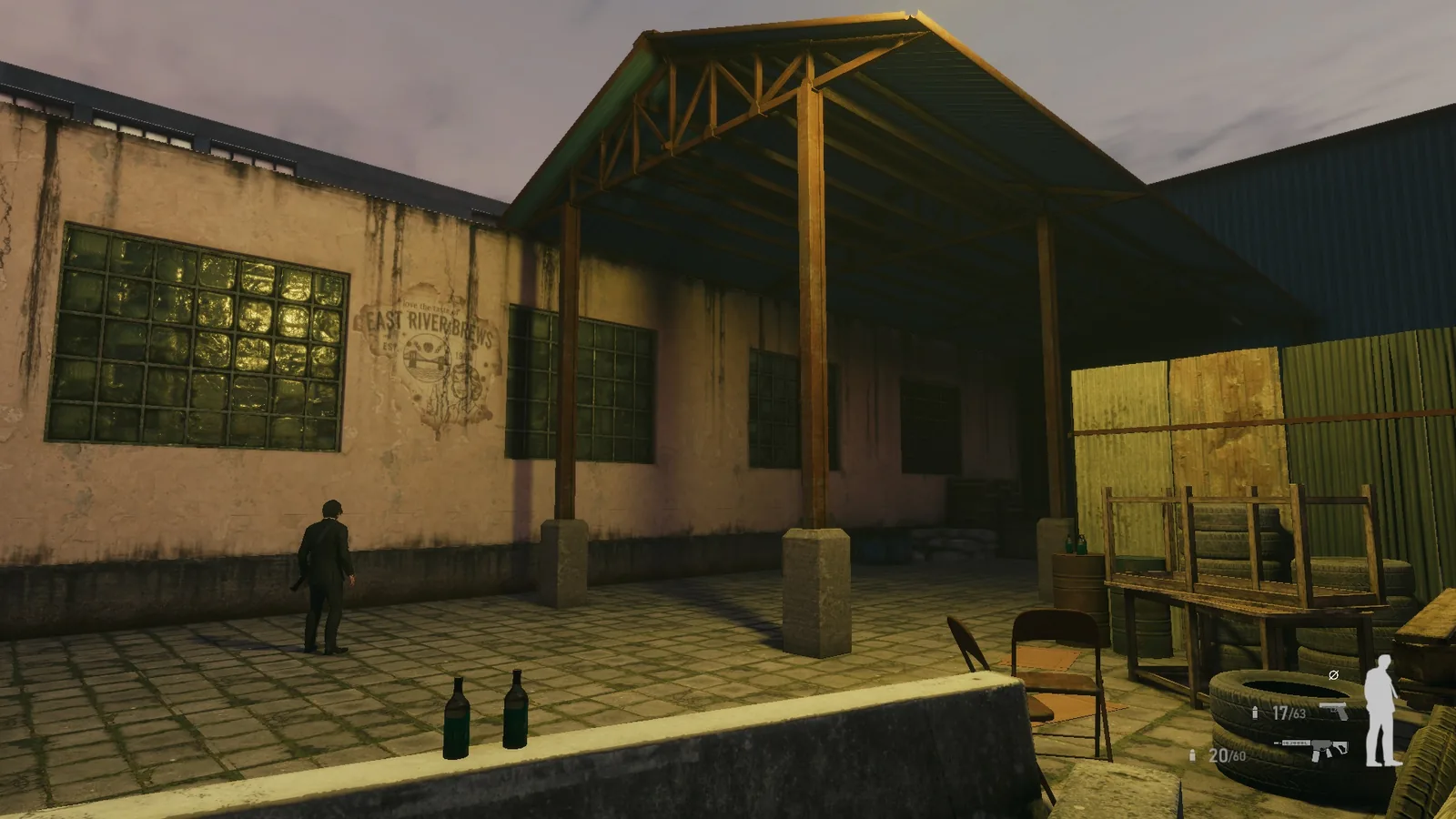 Exterior of the BLACKWOOD warehouse at dusk, with a steel canopy, barred windows, pallets and a lone character in the yard